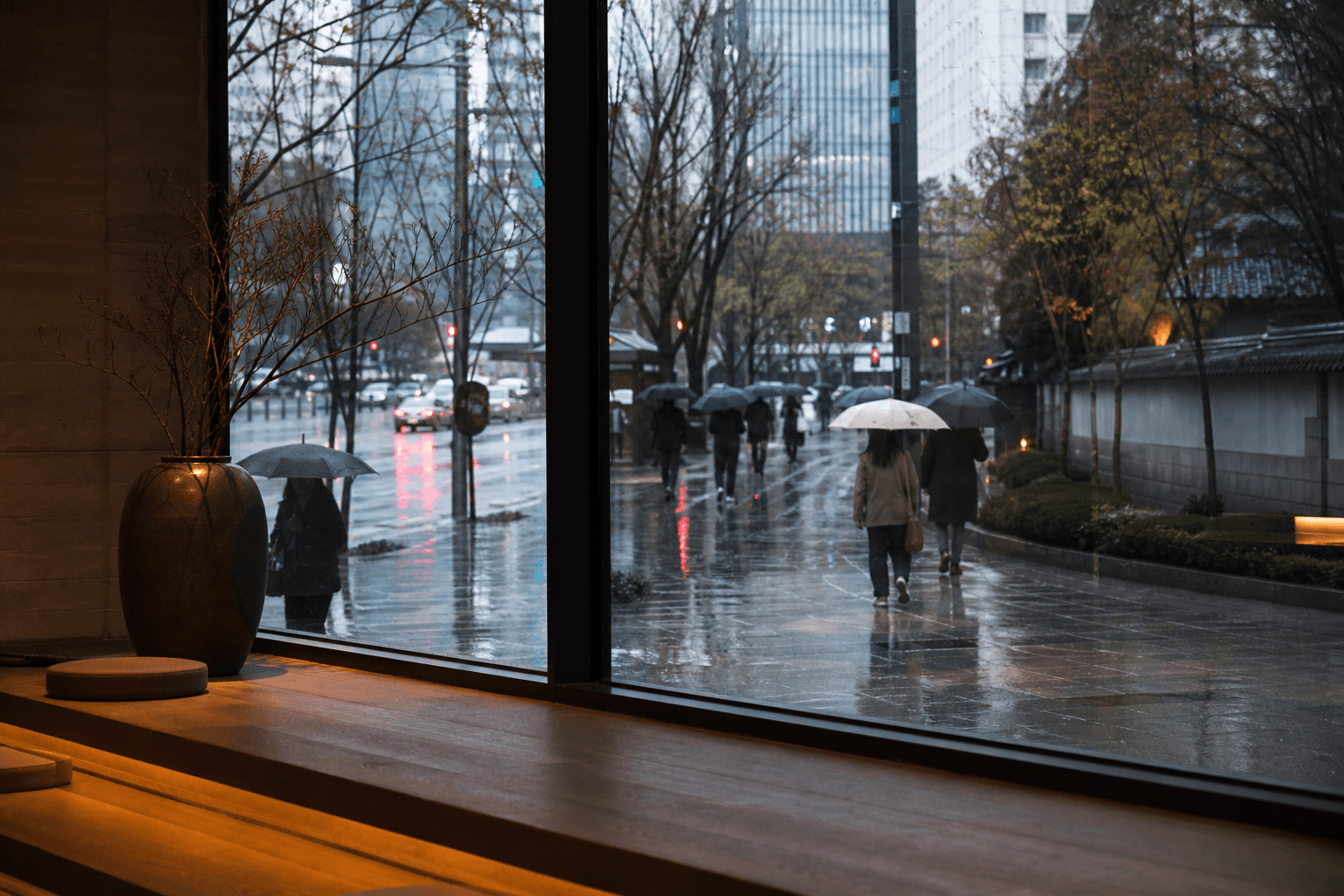 Rainy Seoul pavement and umbrellas seen from a warm indoor window