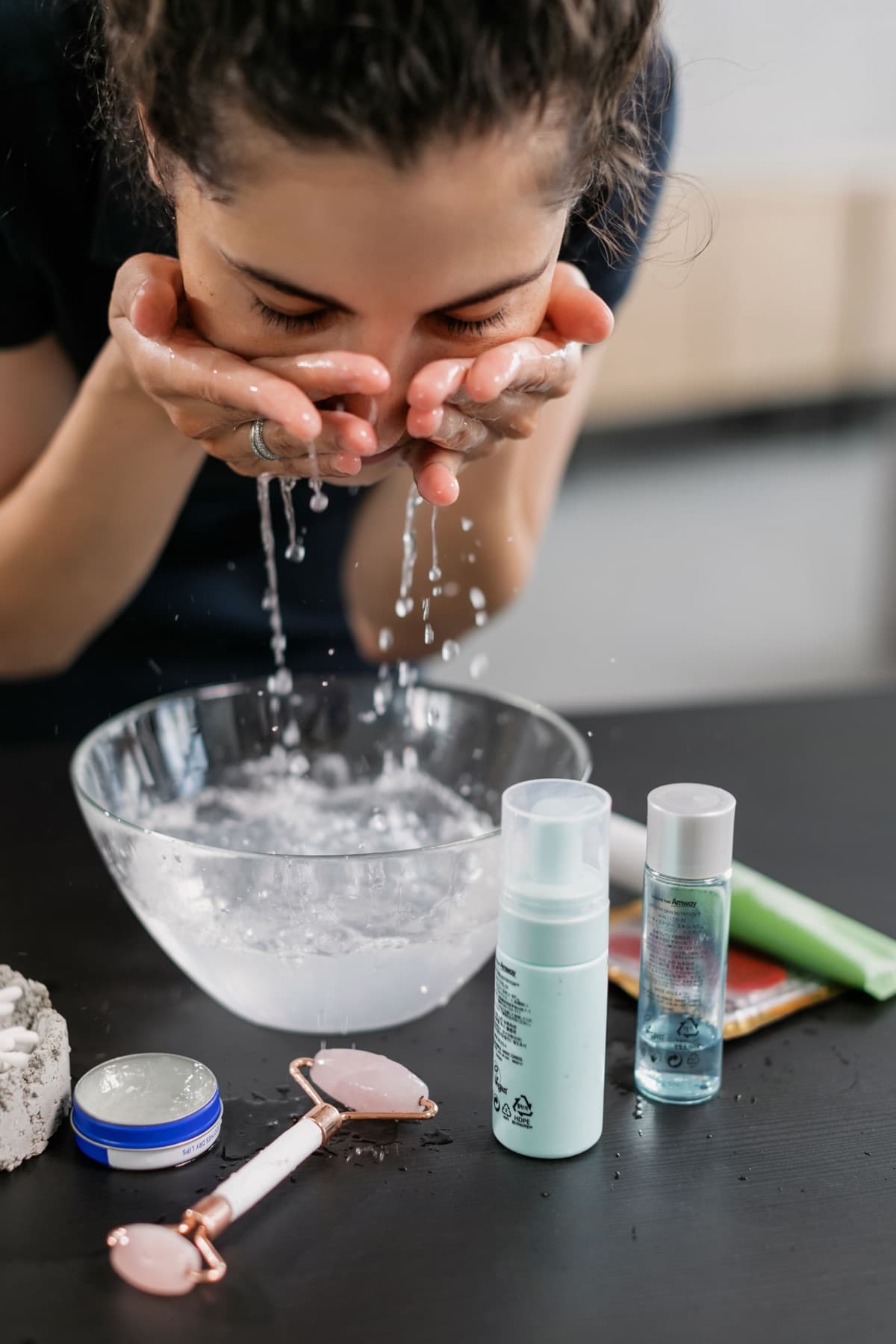 Bathroom counter with cleansing water, skincare bottles, and a face roller after washing