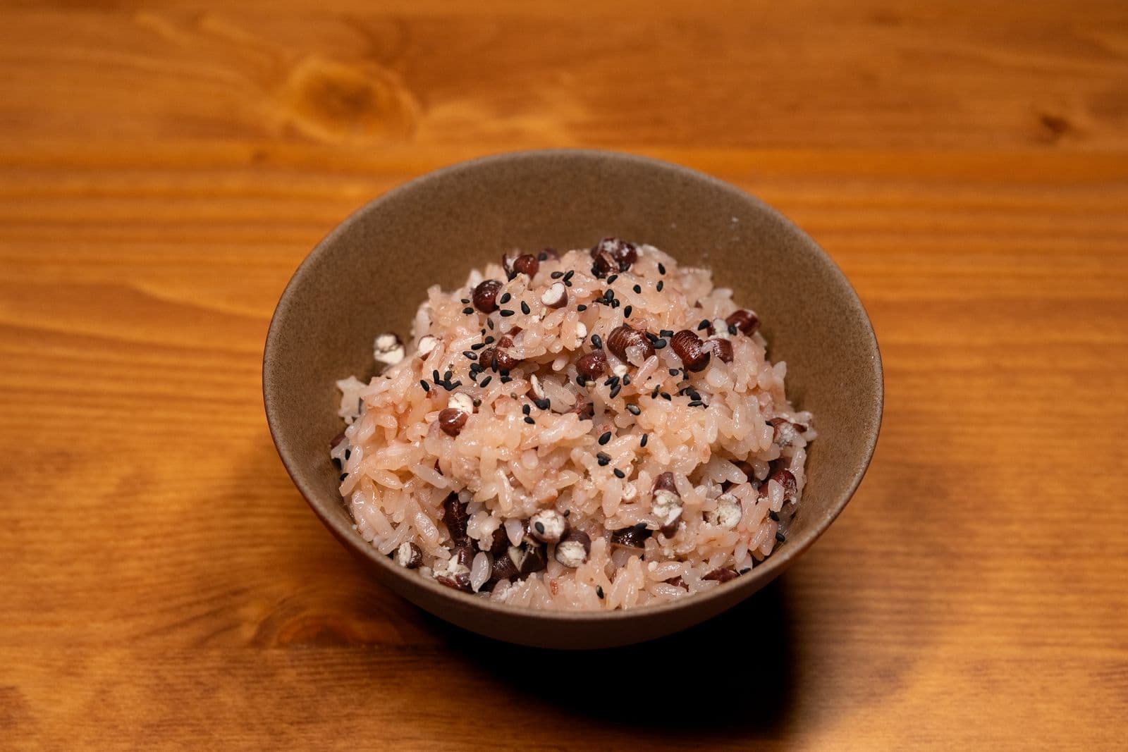 A ceramic bowl of Korean multigrain rice with red beans, job's tears, and black sesame on a wooden table